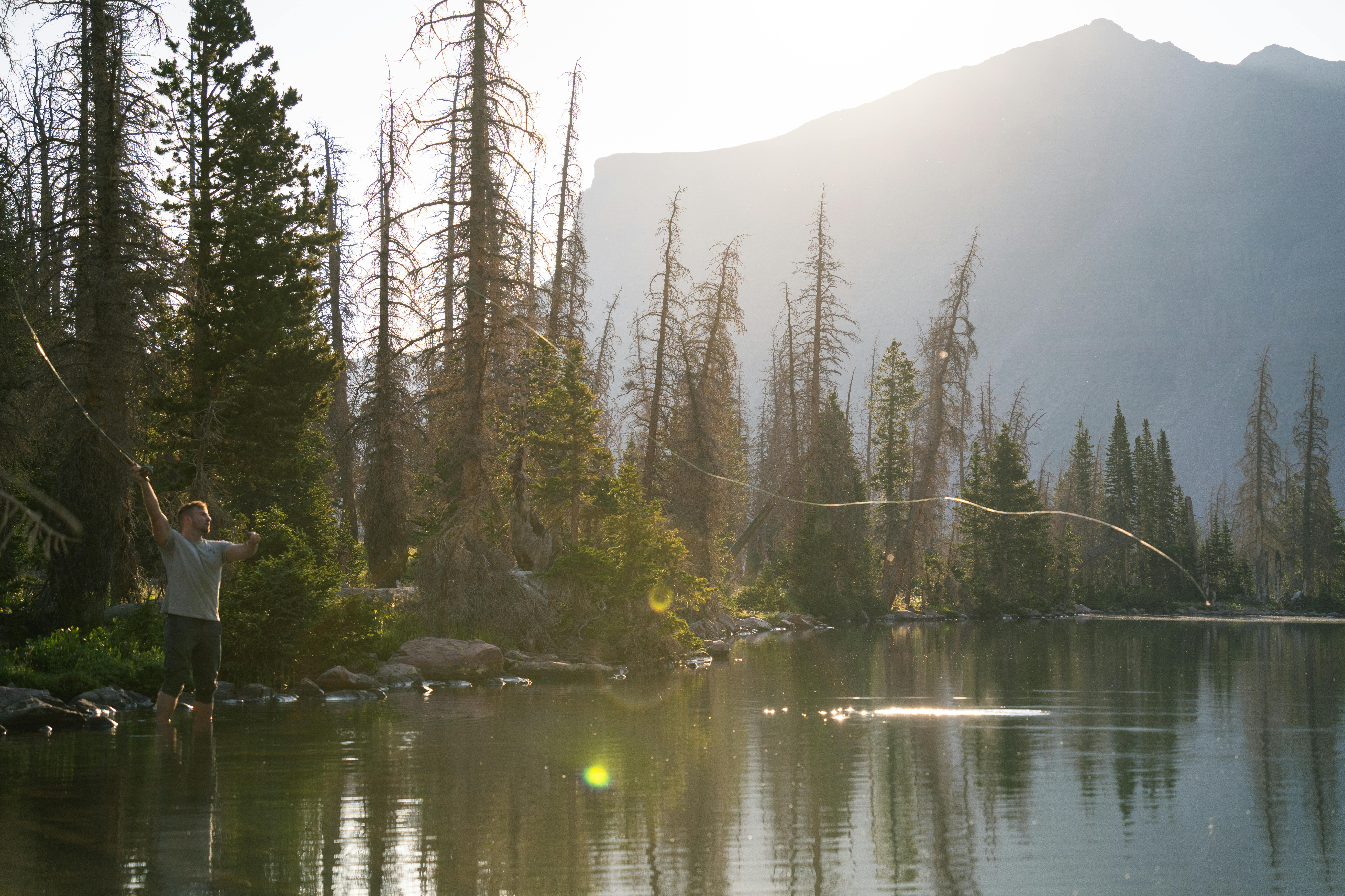 A lone fly fisherman casting his line in a tranquil mountain lake during daylight.