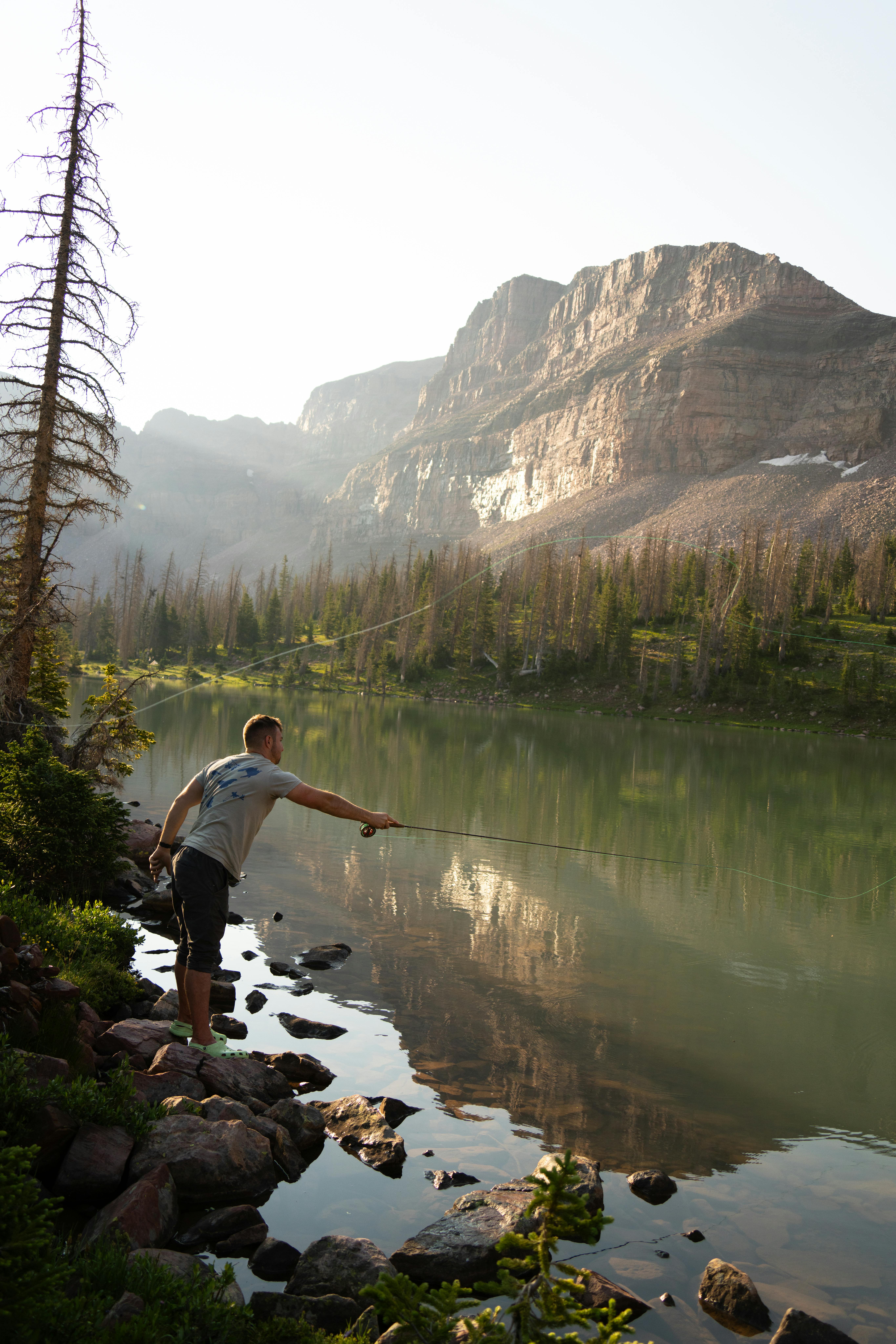 Man fly fishing in a tranquil mountain lake with scenic landscapes at dusk.