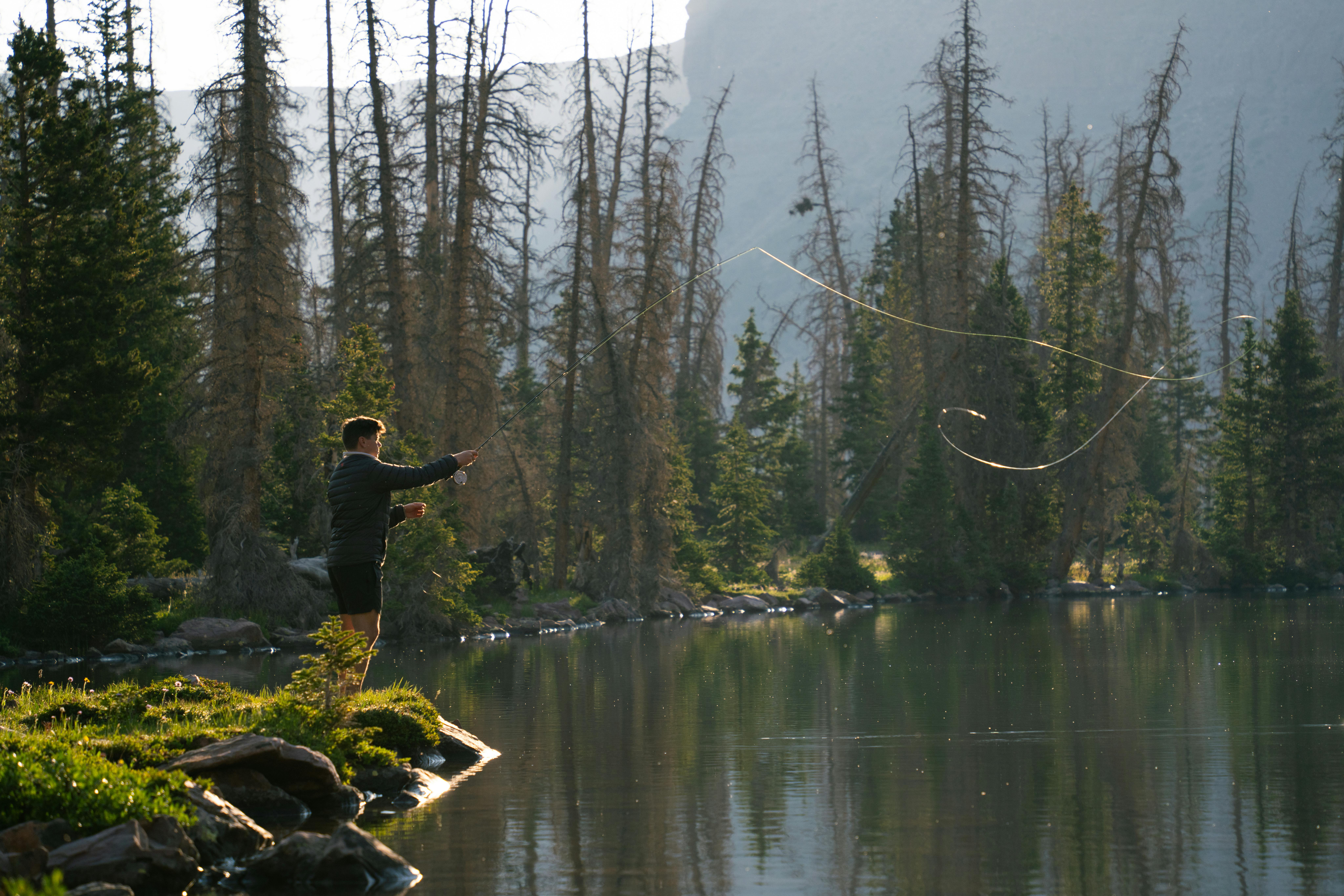 Fly fishing at a serene alpine lake in the wilderness during early morning light.