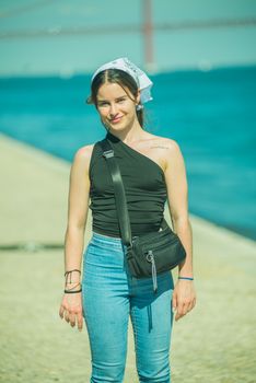 A cheerful young woman stands by the ocean on a sunny day, embracing leisure and style.