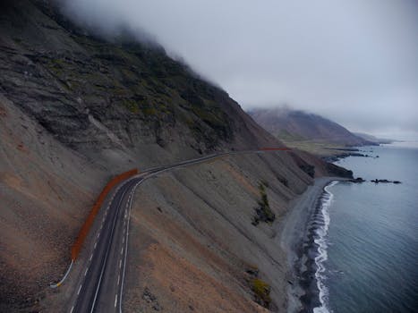A breathtaking aerial view of a coastal road in Iceland, featuring dramatic landscapes and moody skies.