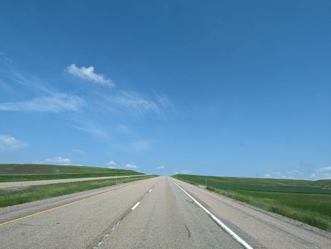 A straight highway disappearing into the horizon under a clear blue sky.