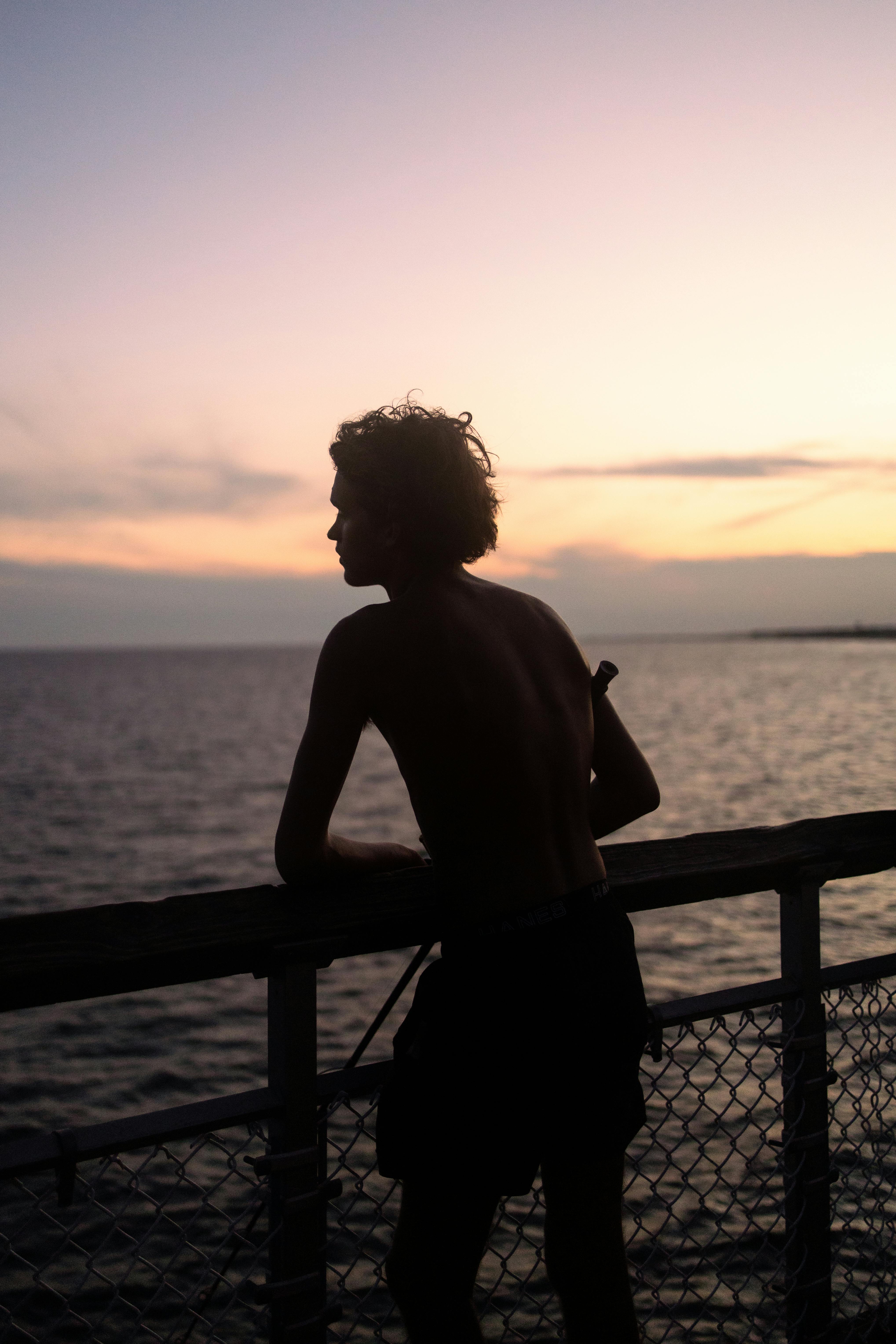 A person silhouetted against a vibrant ocean sunset from a pier.