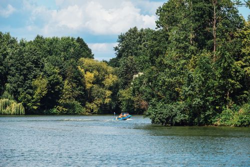 Free A peaceful scene of a boat gliding on a lake surrounded by lush green trees in summer. Stock Photo