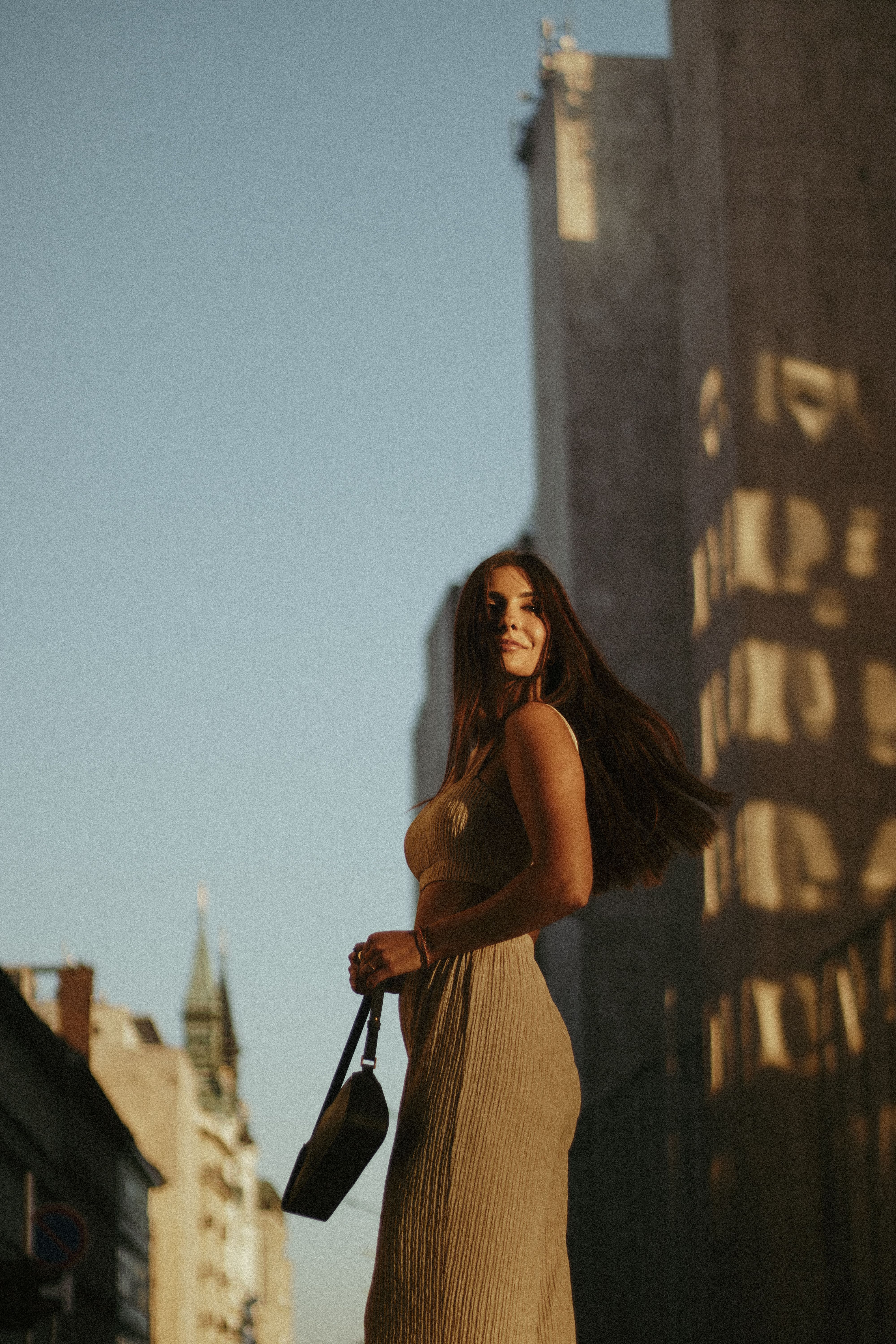 A stylish woman walks through a sunlit city street, exuding glamour and confidence.