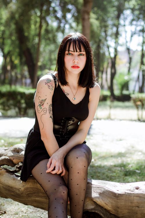 Free Portrait of a fashionable woman with tattoos sitting on a tree in a sunny park. Stock Photo