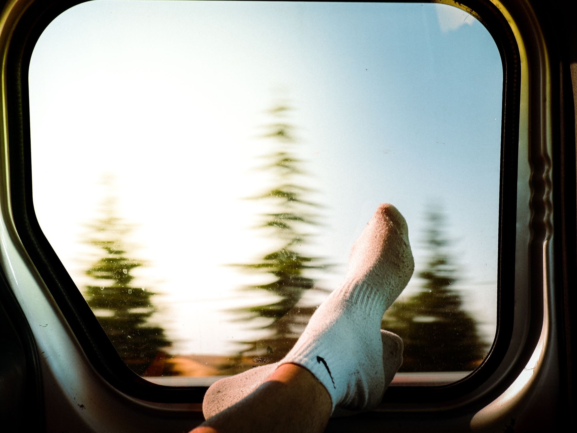 Feet in socks propped up by a car window during a road trip, representing travel leg comfort