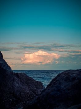 Beautiful coastal view at sunset with dramatic clouds and rocky foreground.