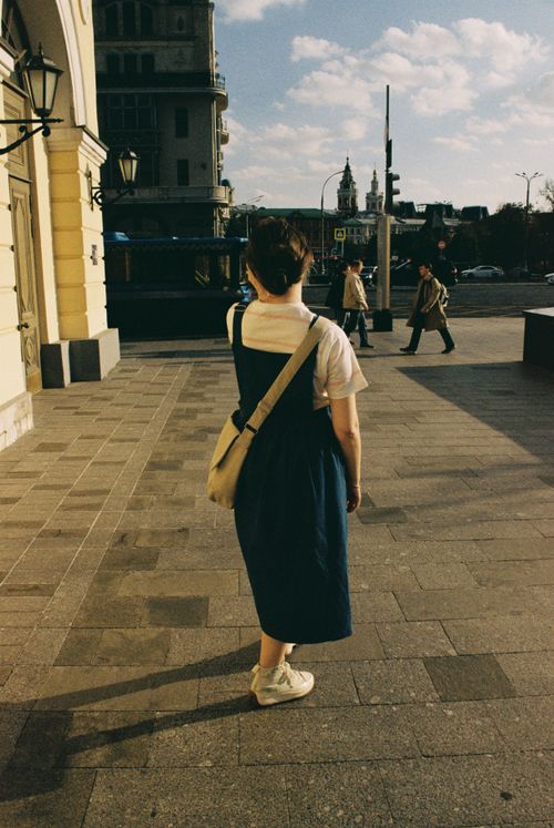 Free A woman stands on a city street with buildings and pedestrians in the background. Stock Photo