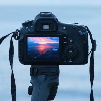 A DSLR camera captures a colorful ocean sunset on its display, set on a tripod.