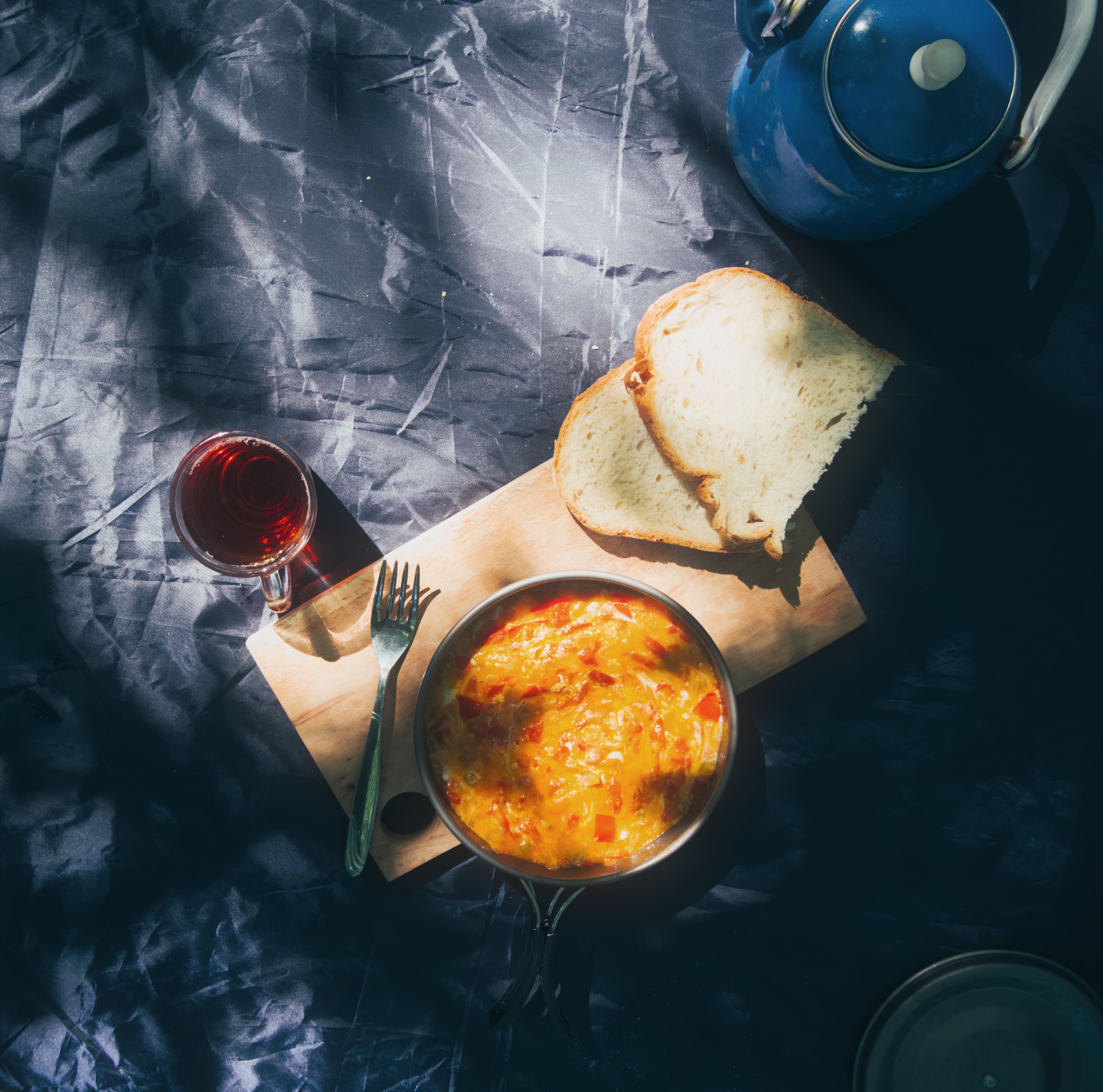 A cozy outdoor breakfast setup with an omelette, bread, and tea on a wooden board.