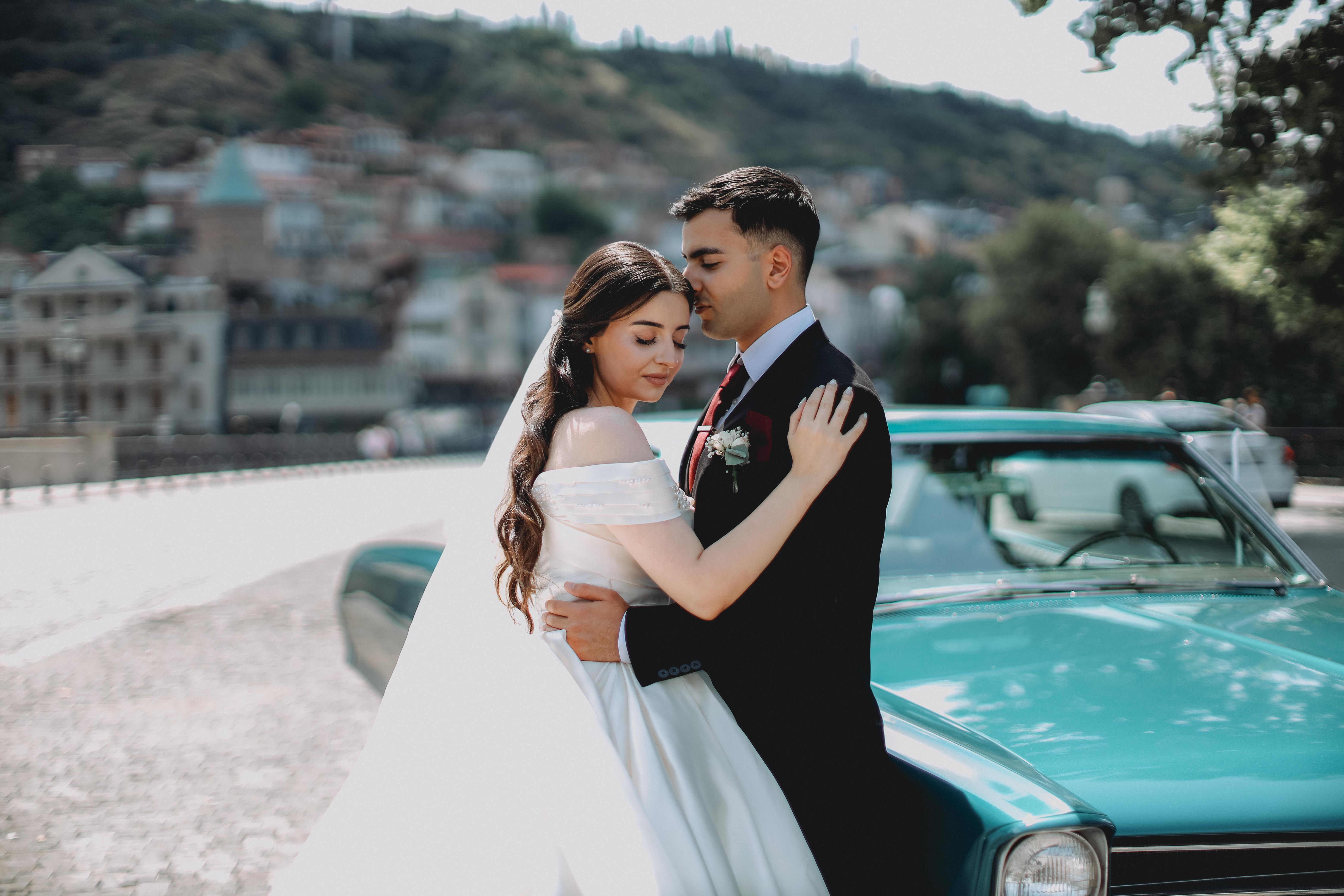 a bride and groom pose in front of a classic car