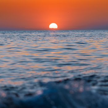 A vibrant sunset over a calm ocean with a clear, colorful sky reflecting on the water.