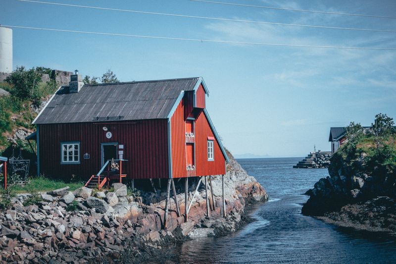 A red wooden house with white trim on a rocky shore beside a narrow inlet of the sea