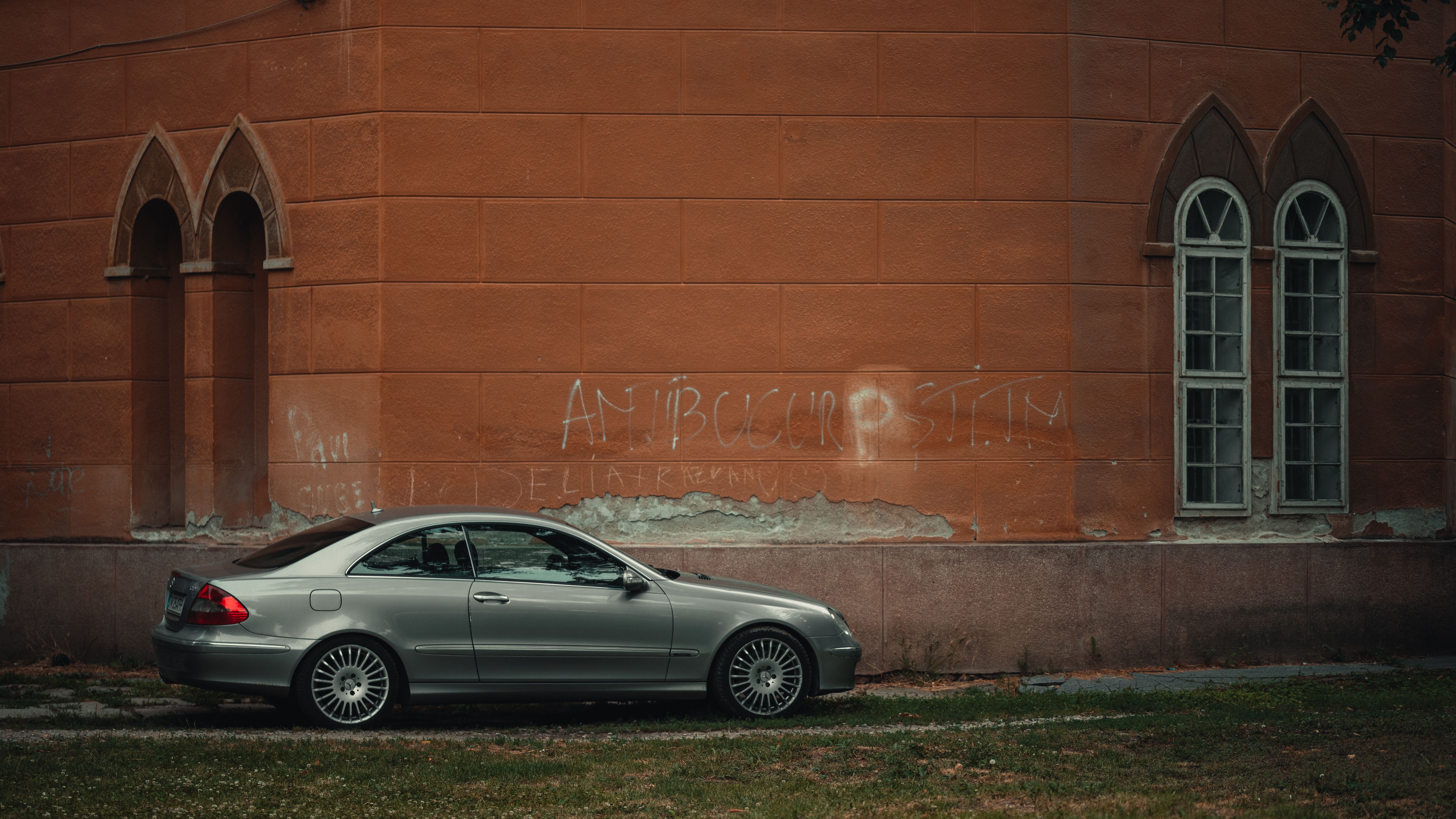 A classic car parked beside a historic architectural building with graffiti on the wall.