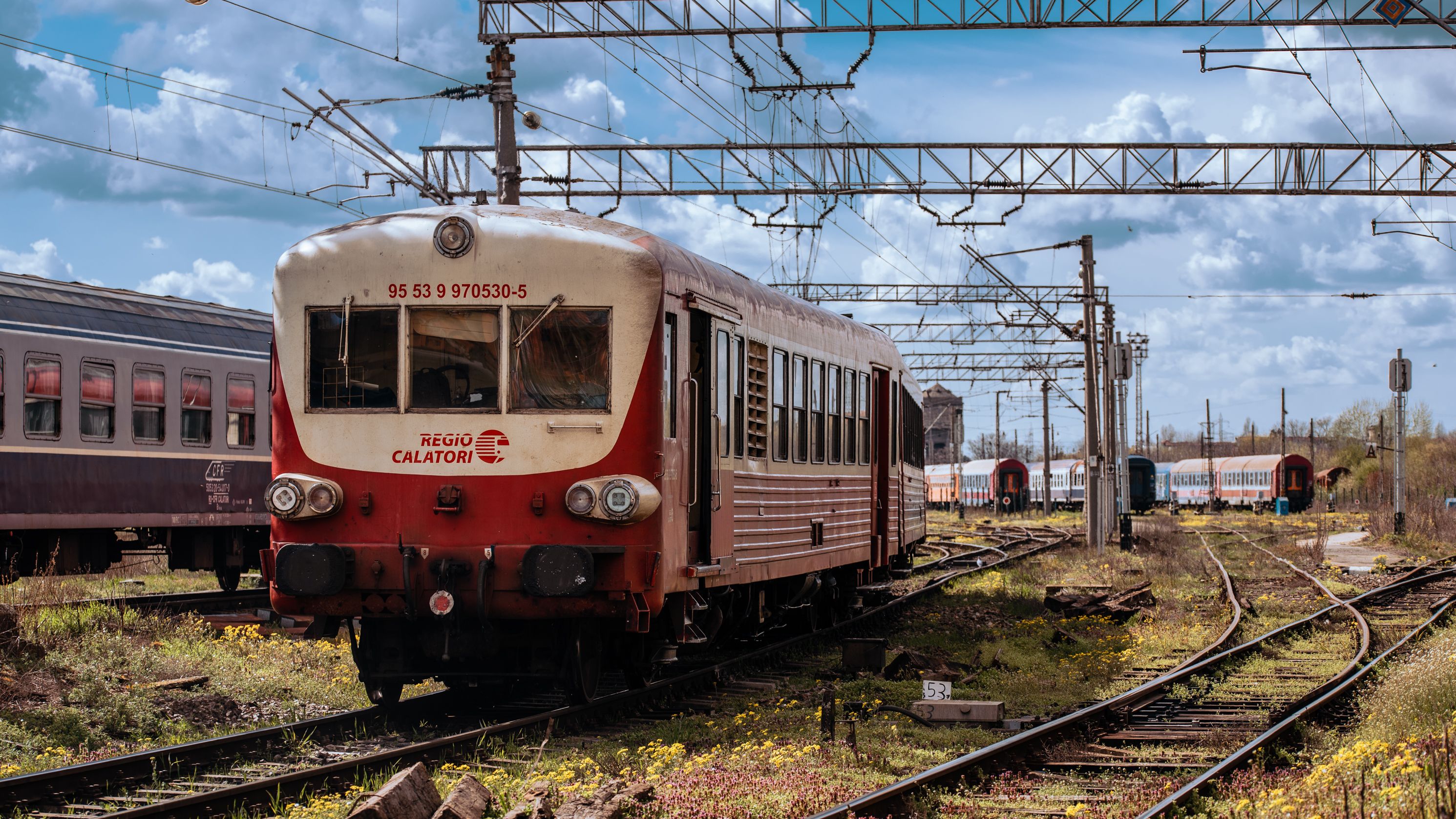 Vintage train and railcars at a station with overhanging wires.