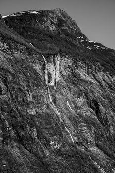 Stunning black and white photo of Geiranger Fjord's rocky landscape and waterfall.