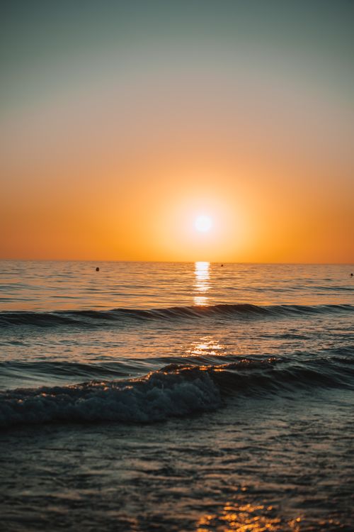 Free A beautiful sunset over the ocean with calm waves and an orange glow. Stock Photo
