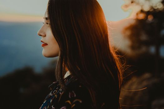 A captivating side portrait of a woman at sunset with a serene landscape in the background.