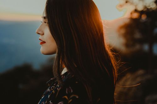 Free A captivating side portrait of a woman at sunset with a serene landscape in the background. Stock Photo