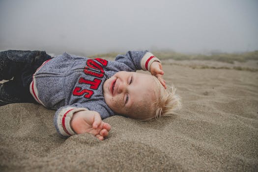 在雾蒙蒙的海滩上，可爱的孩子躺在沙滩上微笑着，享受着有趣的一天