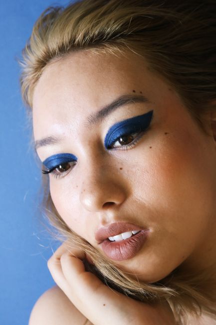 Close-up portrait of a woman highlighting striking blue eye makeup and soft expression.