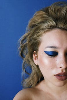 Close-up portrait of a woman with striking blue eye makeup and softly curled hair against a matching blue background.