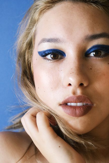 Striking close-up of a woman with bold blue eye makeup against a blue background.