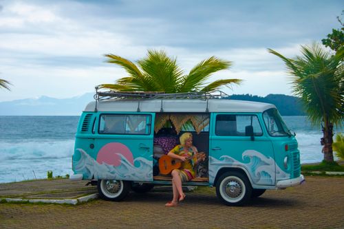 Free Colorful camper van on a tropical beach with a woman playing guitar, ocean view. Stock Photo