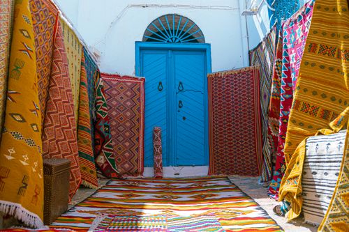 Free Vibrant display of traditional Tunisian carpets at a blue door entrance in Carthage, Tunisia. Stock Photo