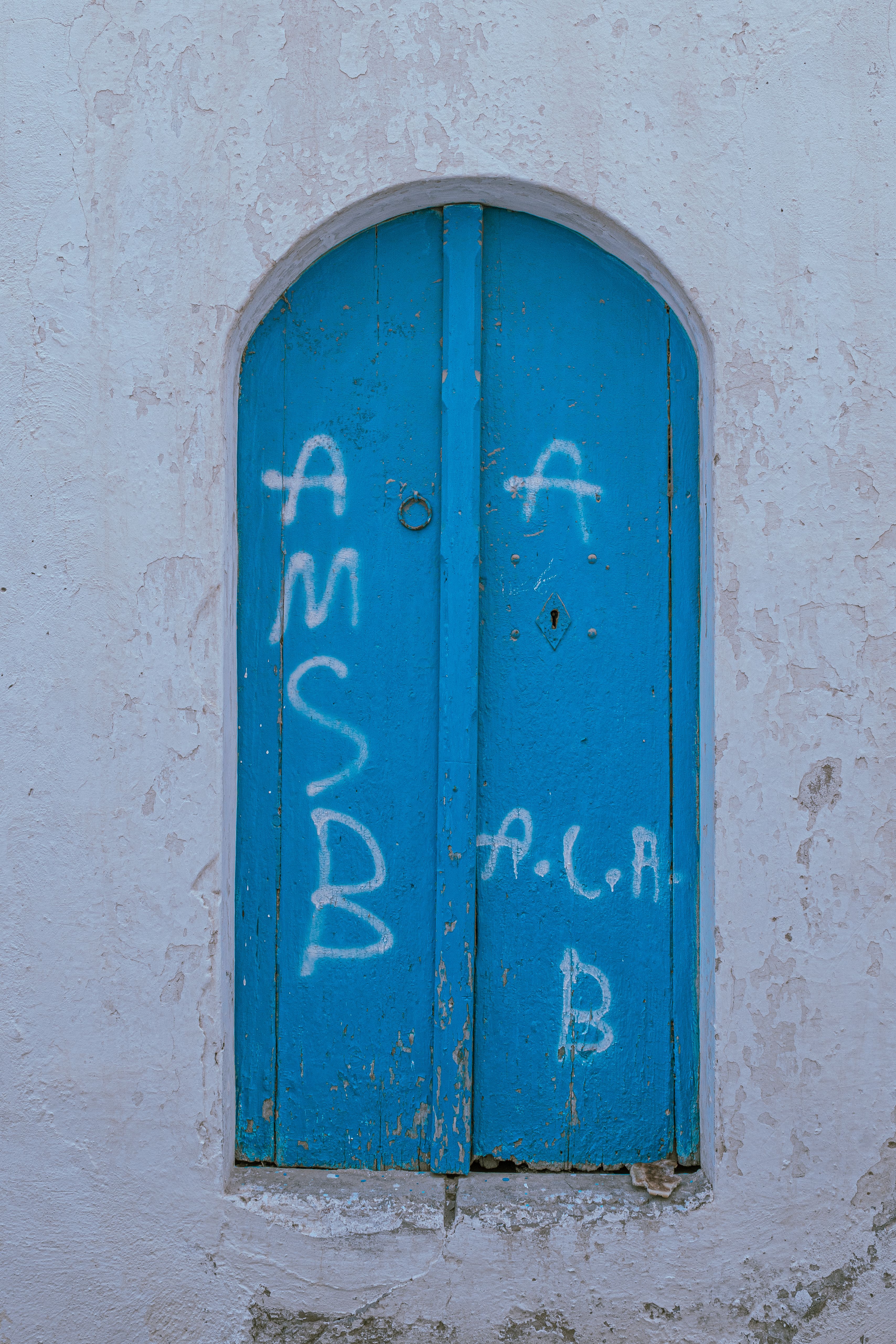 A weathered blue door with graffiti in Carthage, Tunis Governorate, Tunisia, evokes rustic charm.