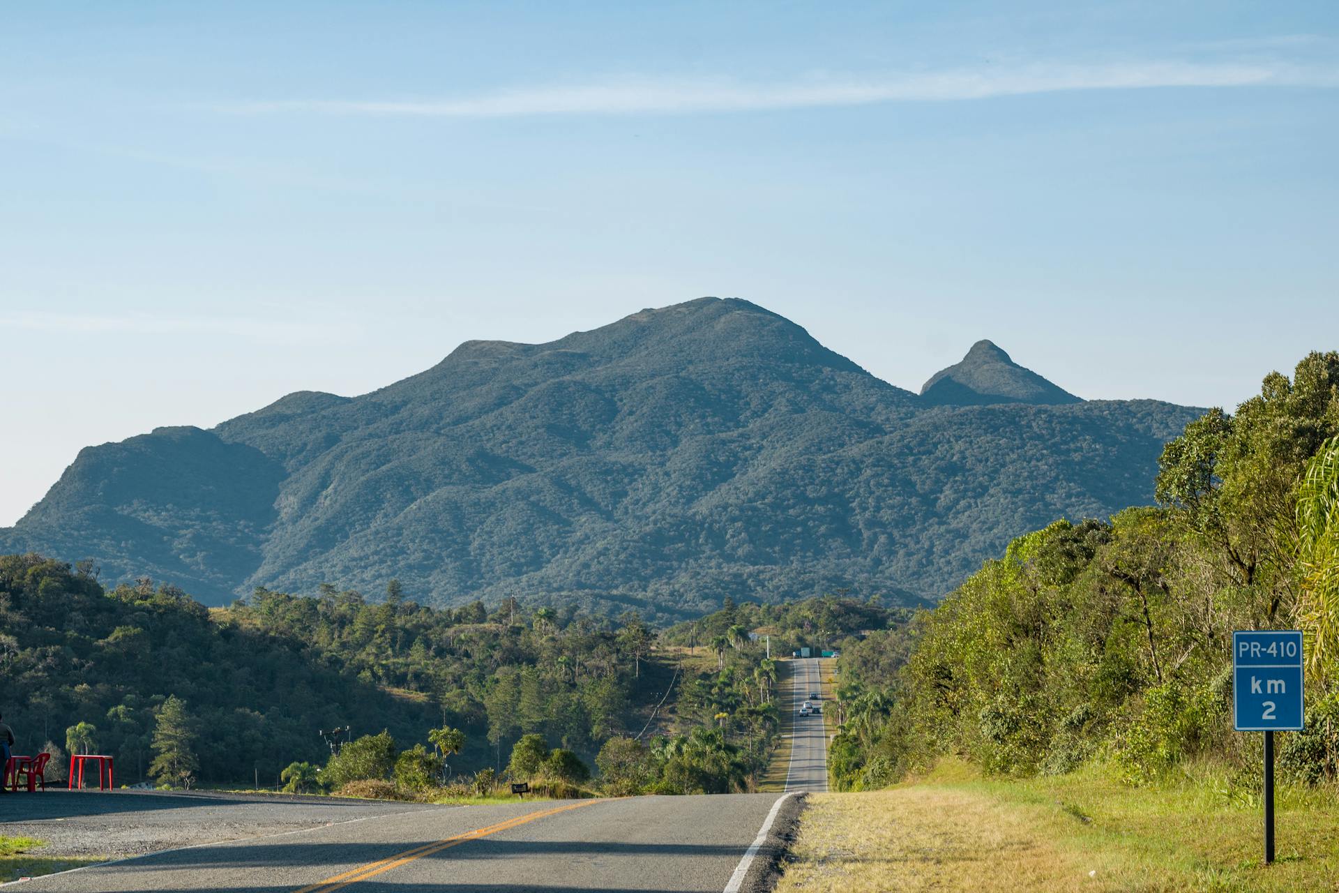 Long road leading to lush green mountains under clear blue sky. Perfect for travel and adventure themes.