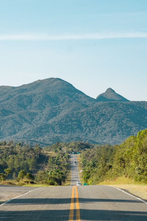 Free Long road stretching towards lush green mountains under a clear blue sky. Stock Photo
