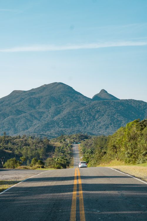 Free A scenic road stretches towards towering green mountains under a clear blue sky. Stock Photo