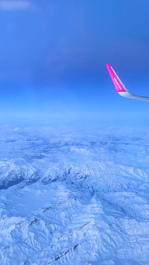 Free Aerial shot of snowy mountains from an airplane window with a bright pink wingtip against a clear blue sky. Stock Photo