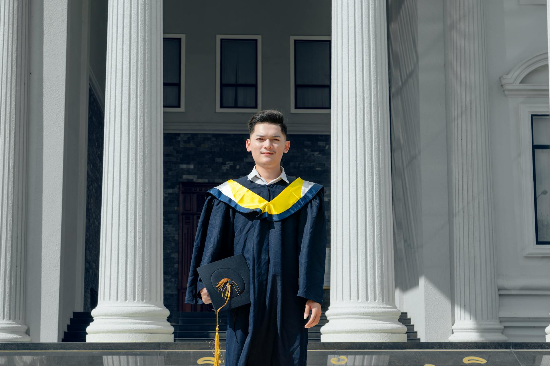 Graduate student posing in cap and gown outside university building with columns.