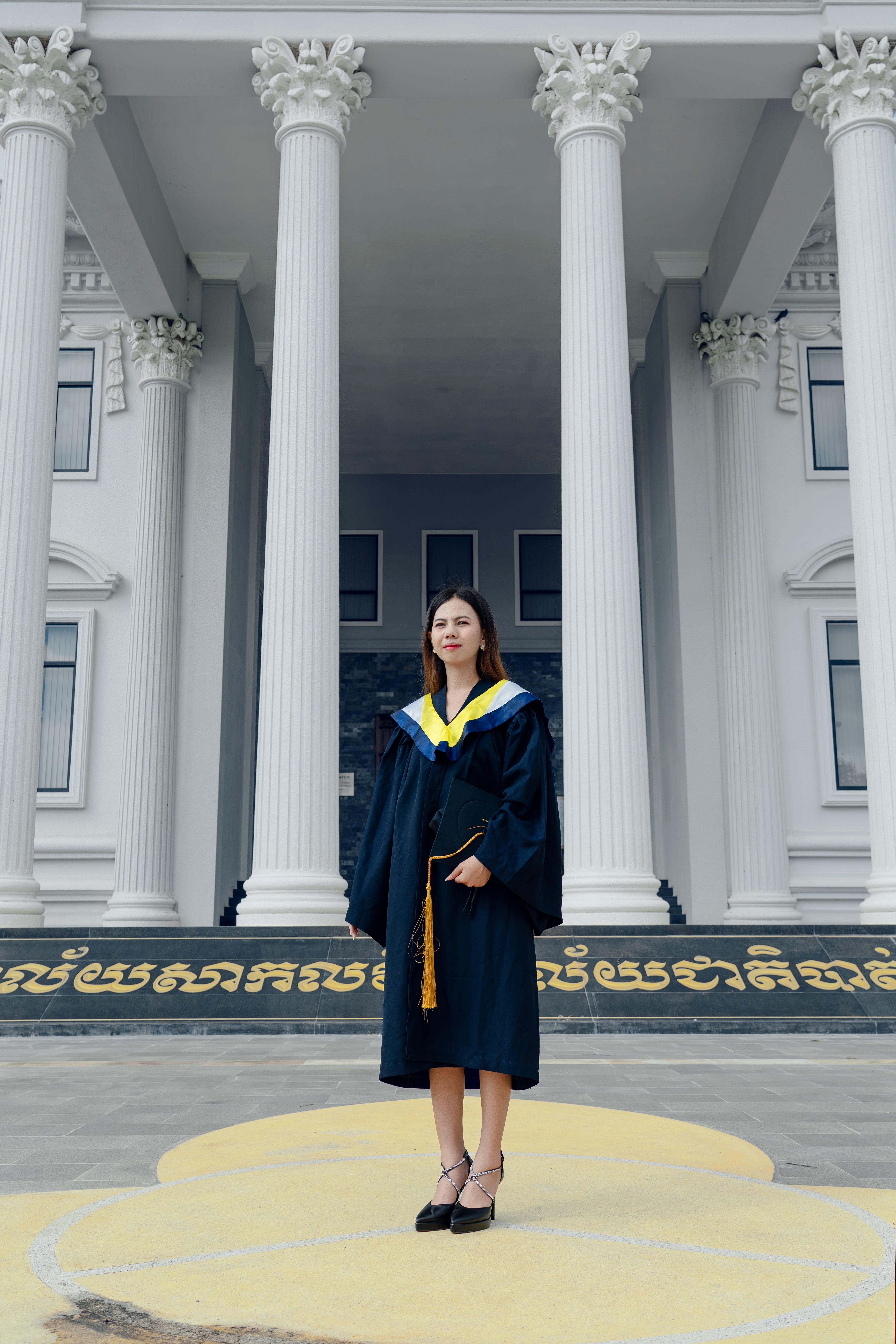 A woman in a graduation gown standing in front of a large building ...