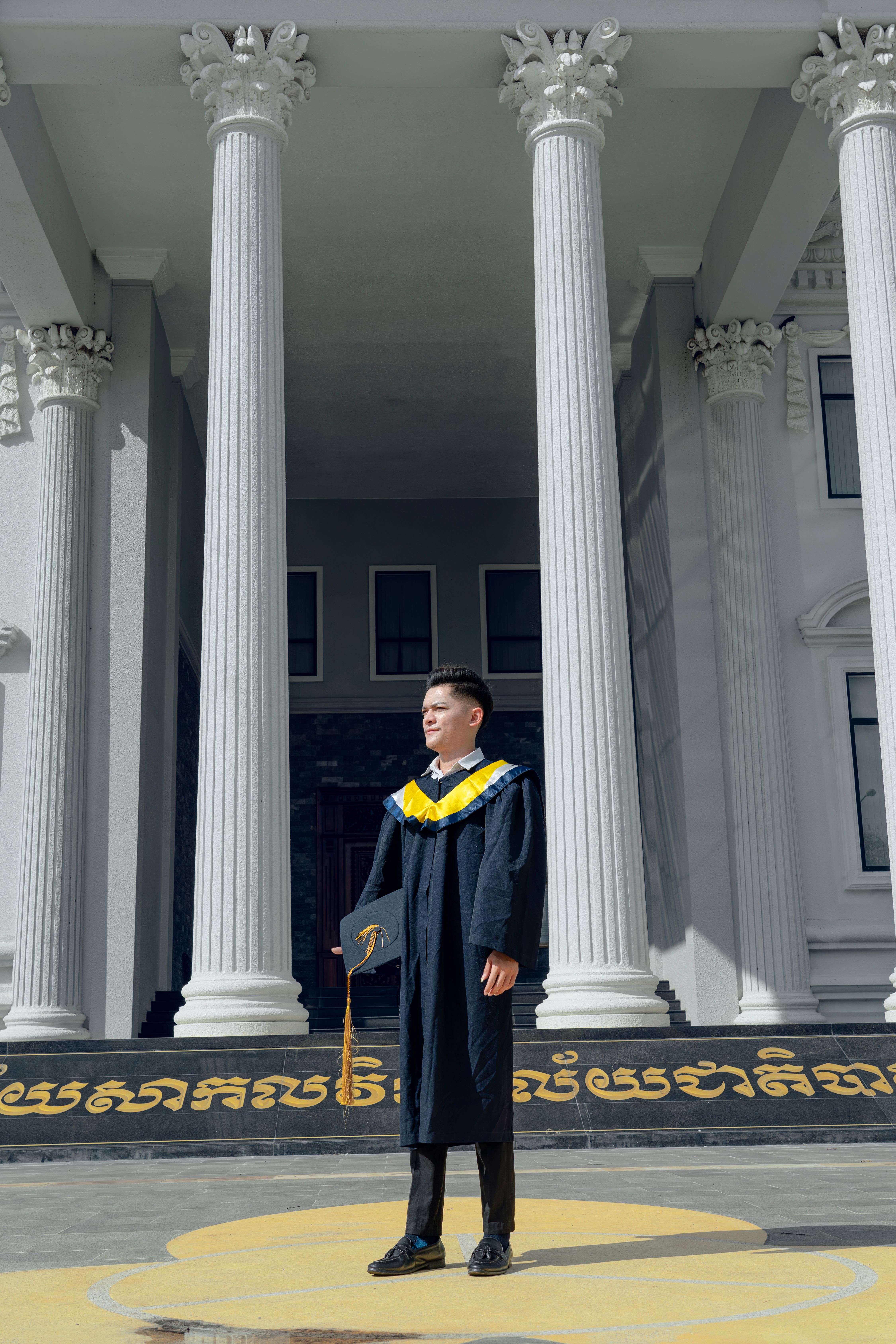 A man in a graduation gown standing in front of a building · Free Stock ...