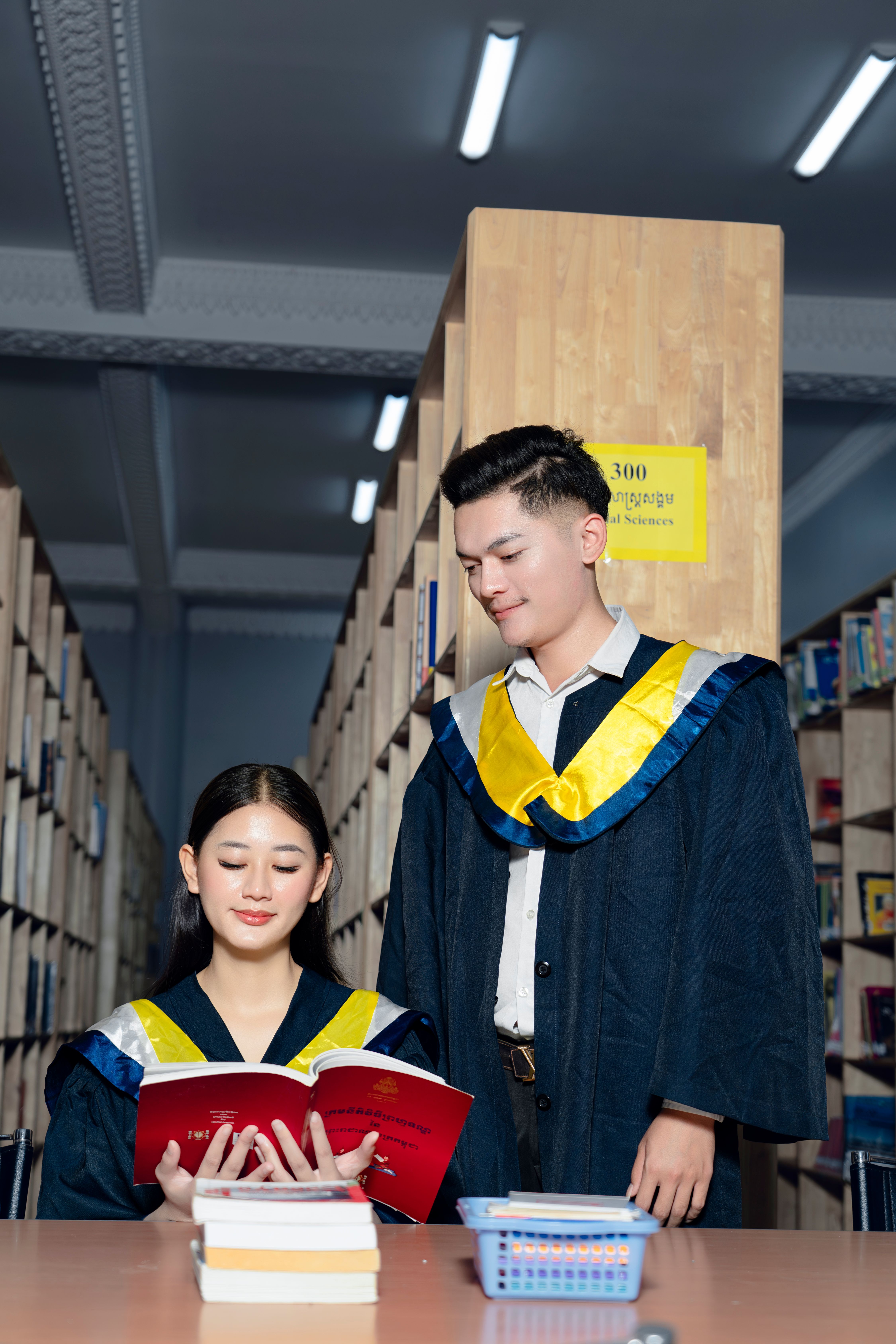 Two students in graduation robes standing in front of books · Free ...