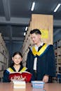 Two students in graduation robes standing in front of books