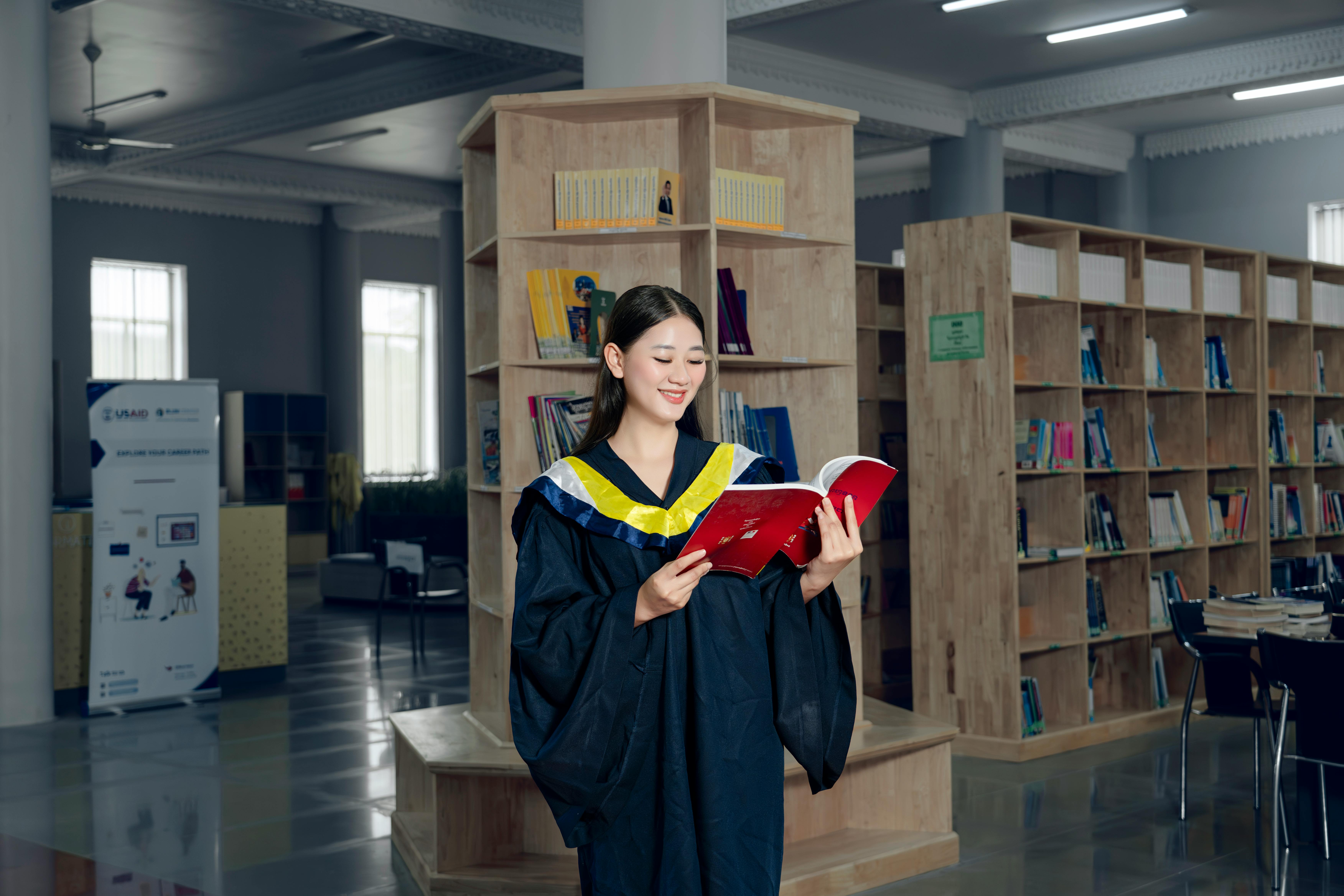 a woman in a graduation gown is holding a book