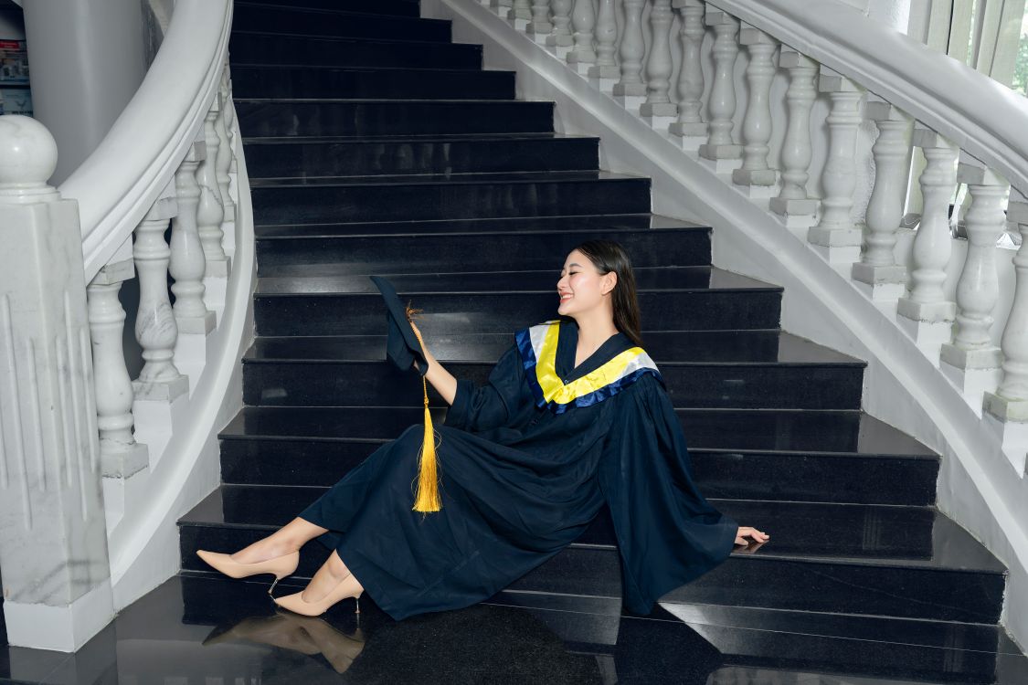 A woman in a graduation gown sitting on stairs · Free Stock Photo