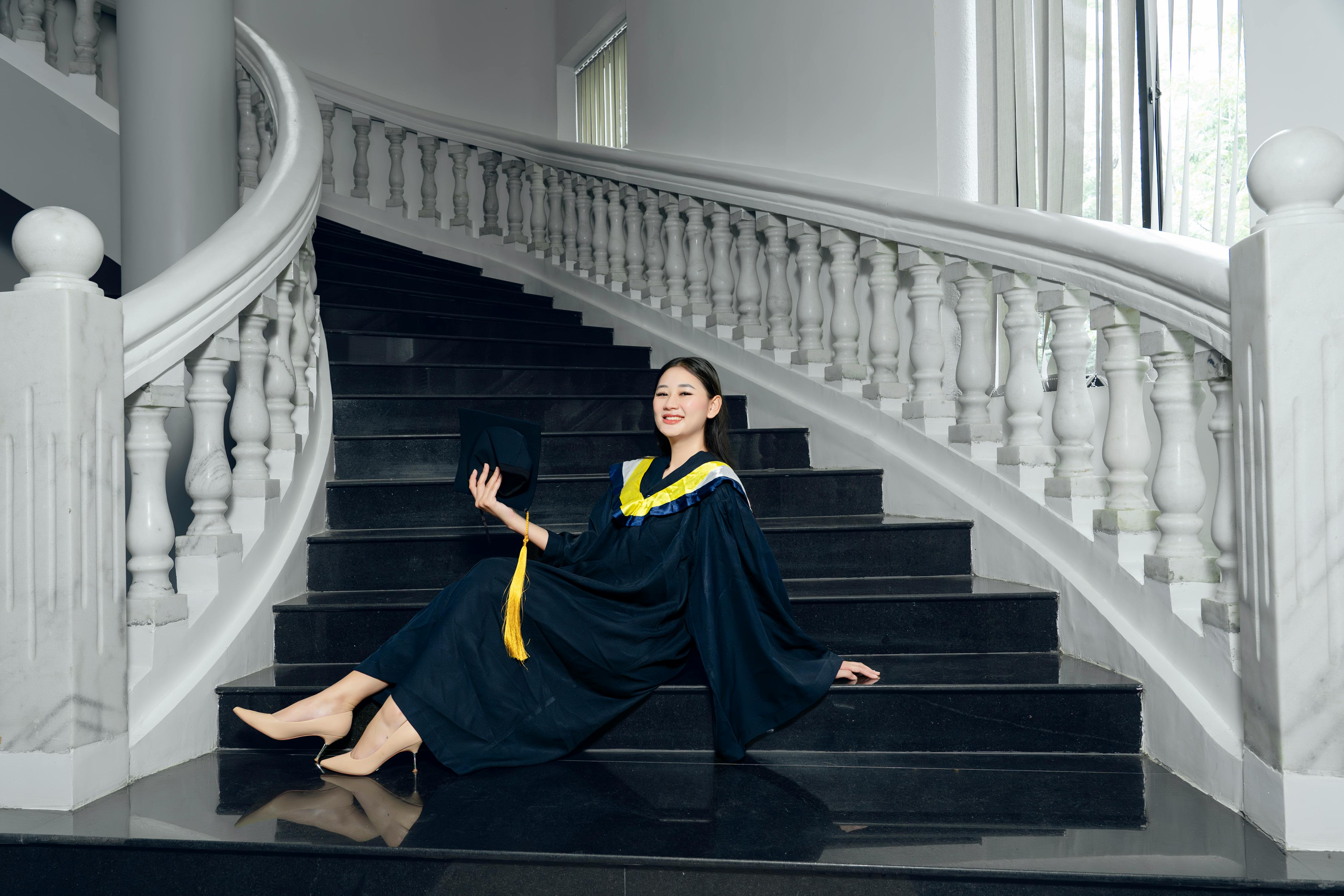 a woman in a graduation gown sitting on stairs