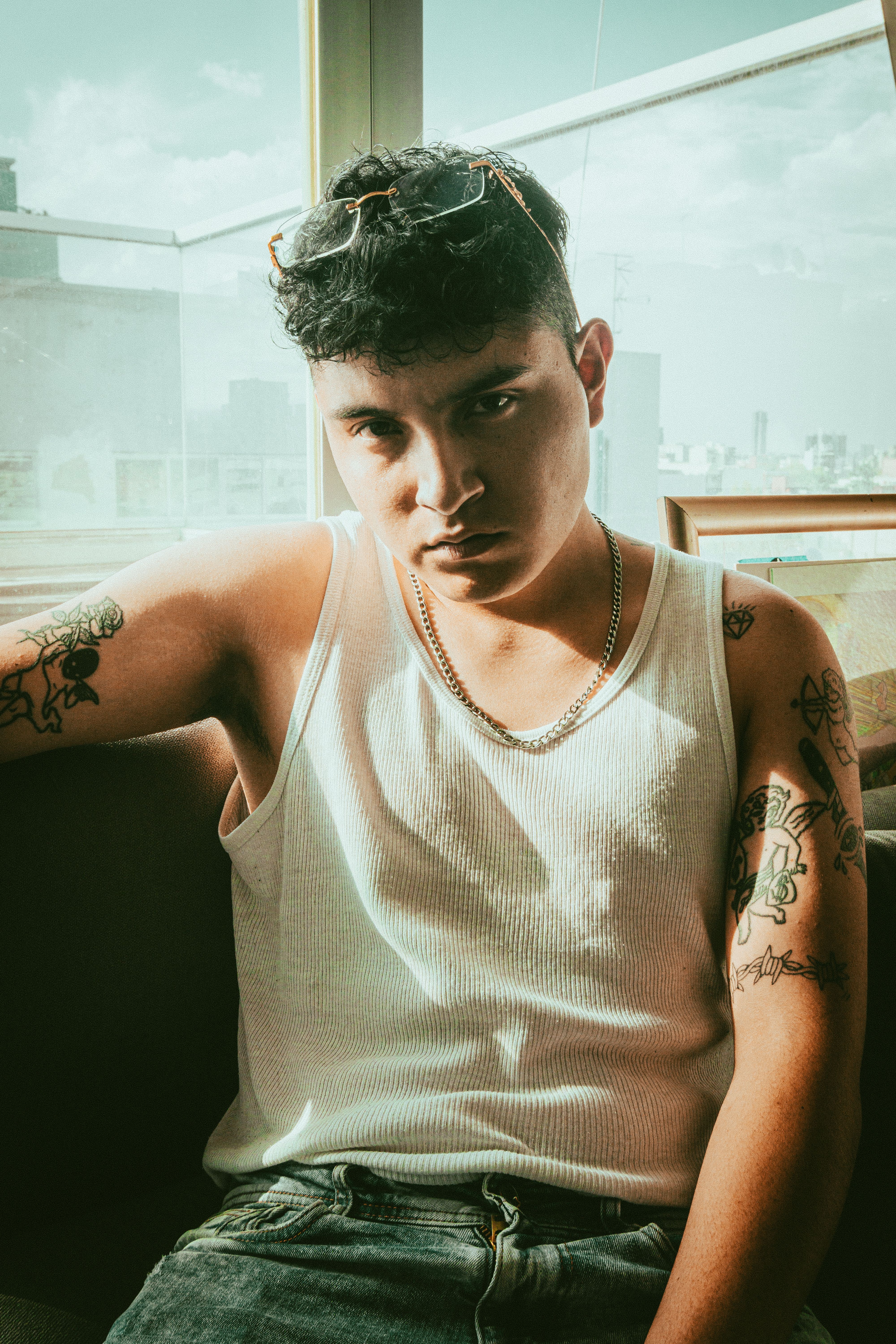 Cool young man with tattoos in a sunlit room, exuding trendy fashion vibes.