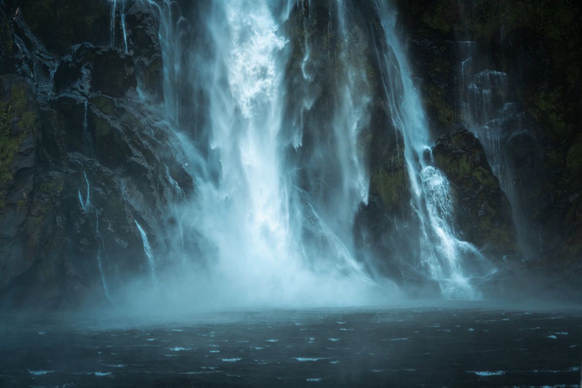A powerful waterfall cascading down a dark rock face into misty water below