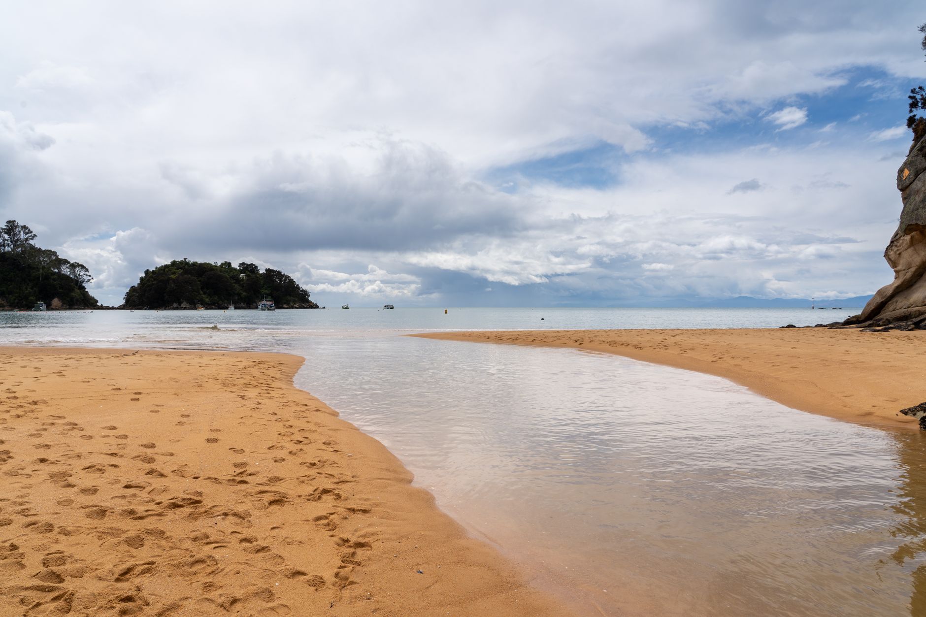 Stunning coastal view of a tranquil beach with golden sands, calm sea, and distant islands under a cloudy sky.