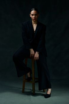 Elegant woman sitting on a stool in a dark suit, exuding fashion and confidence.