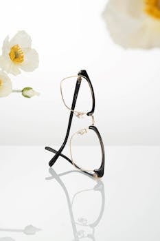 Stylish black and gold eyeglasses with white flowers on a reflective surface.