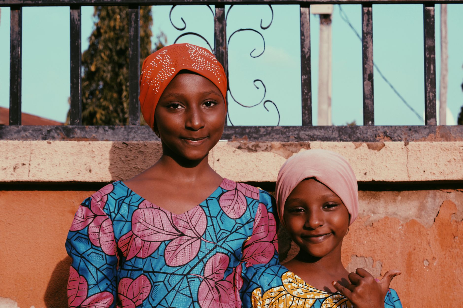 Two girls in colorful traditional Nigerian clothing smiling outdoors in Abuja, Nigeria.