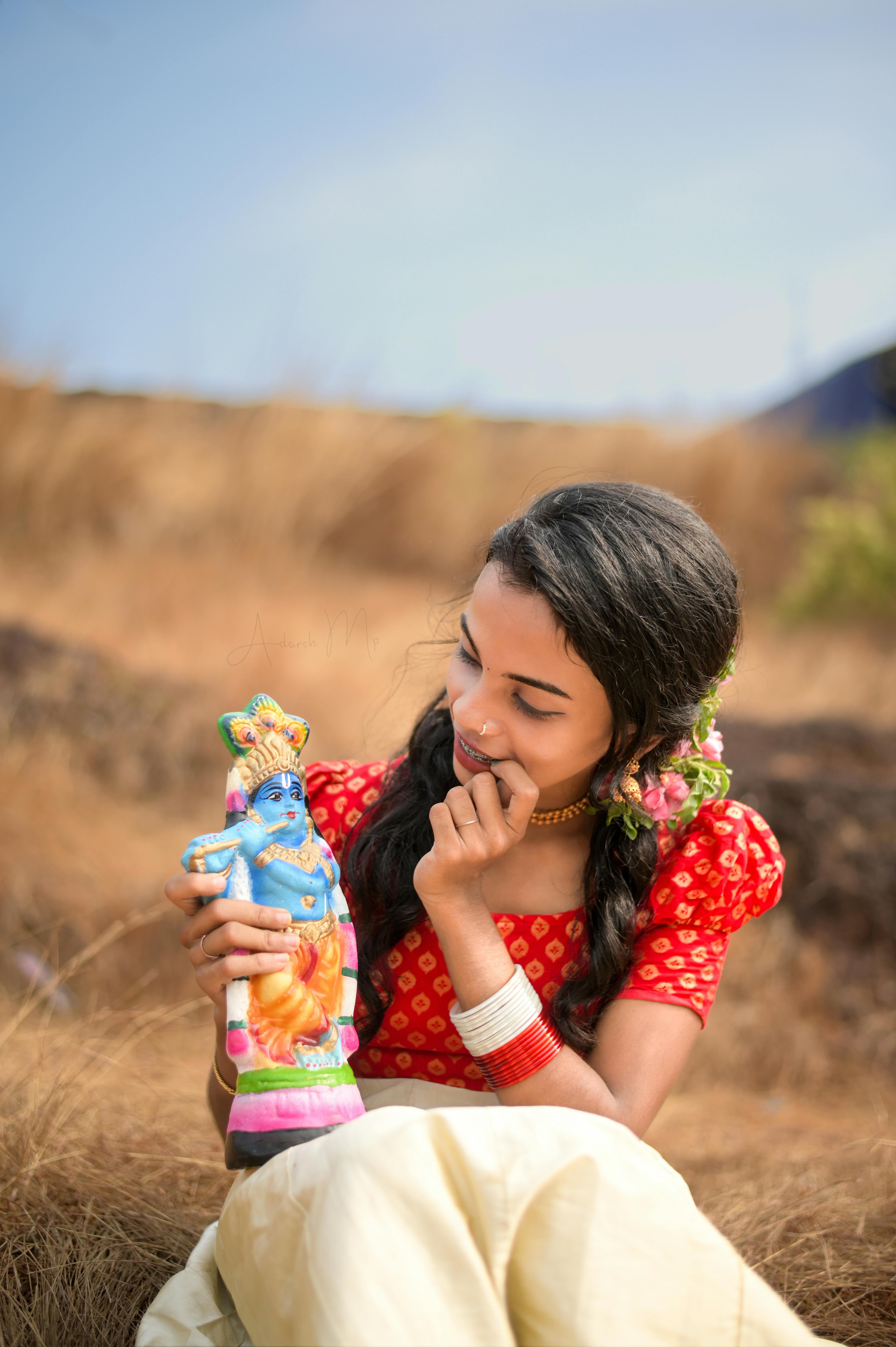 Charming portrait of a young girl in a red dress playing outdoors with a Krishna idol.